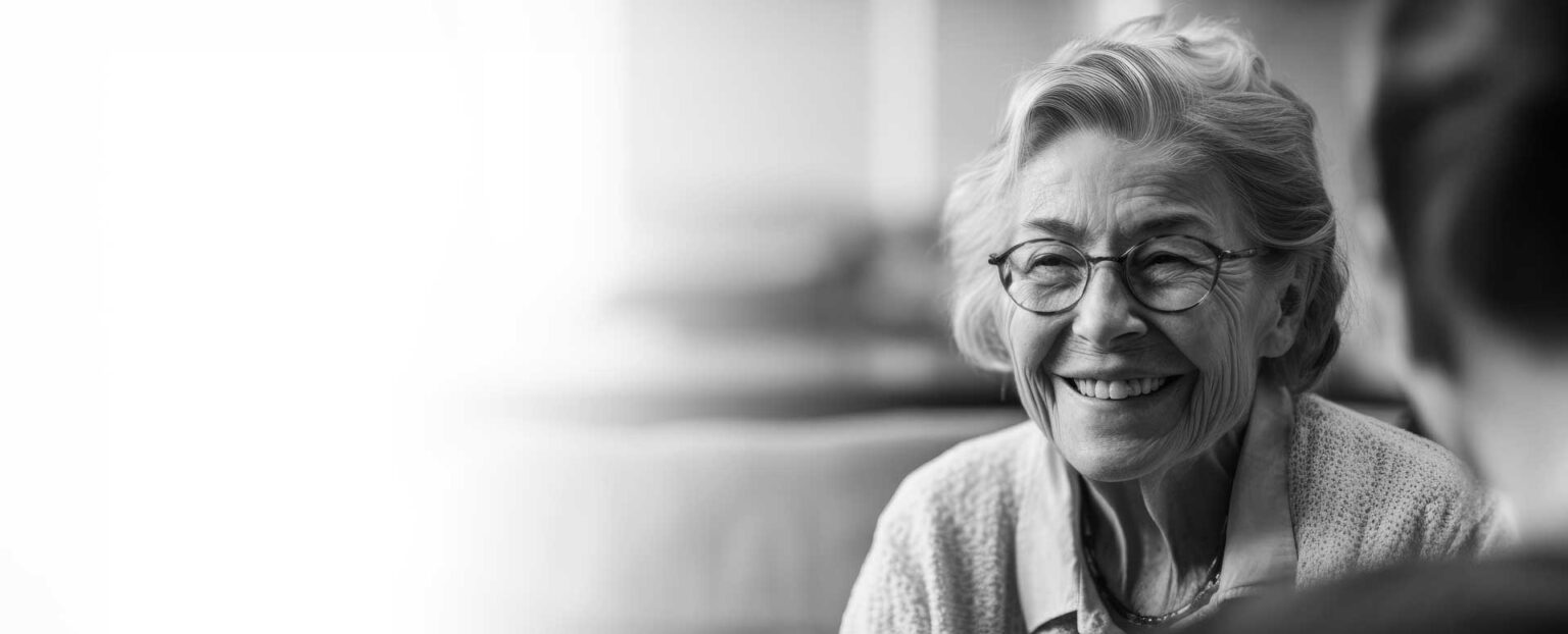 Older woman with glasses sitting and smiling.